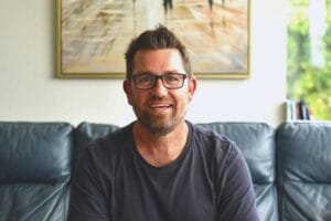 Paul Heron sharing new business tips while working from the couch, smiling at the camera