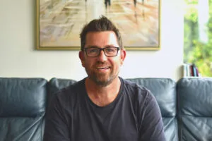 Paul Heron sharing new business tips while working from the couch, smiling at the camera