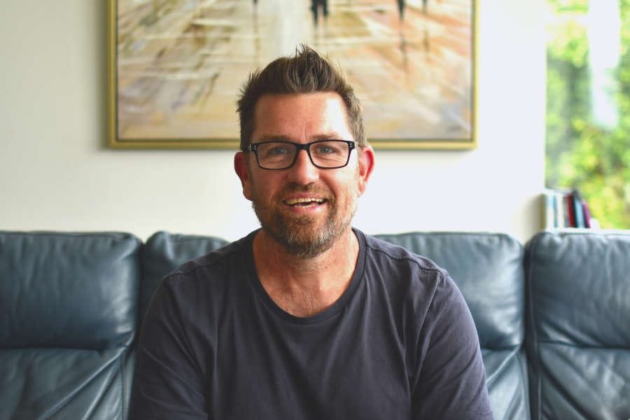 Paul Heron sharing new business tips while working from the couch, smiling at the camera